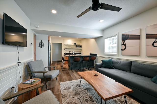 living room featuring hardwood / wood-style floors, ceiling fan, and a textured ceiling