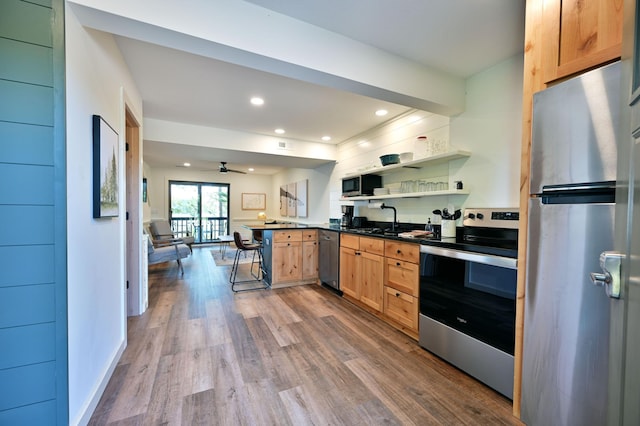 kitchen featuring a kitchen bar, appliances with stainless steel finishes, kitchen peninsula, ceiling fan, and hardwood / wood-style floors