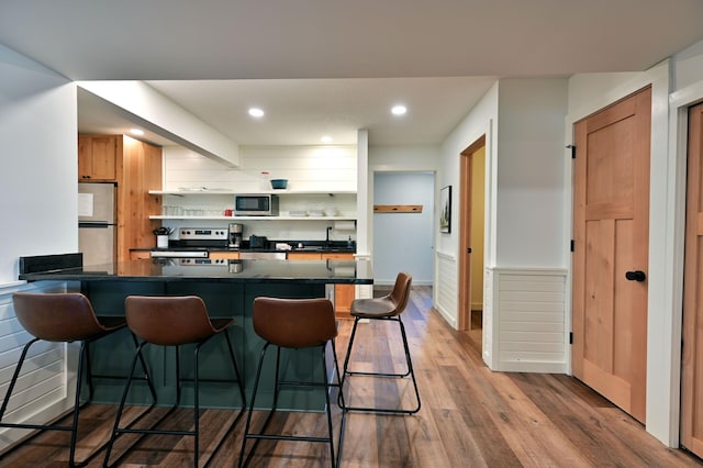 kitchen featuring kitchen peninsula, a breakfast bar, stainless steel appliances, and light hardwood / wood-style flooring