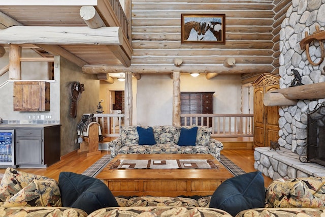 living room featuring rustic walls, light hardwood / wood-style flooring, a stone fireplace, and beverage cooler