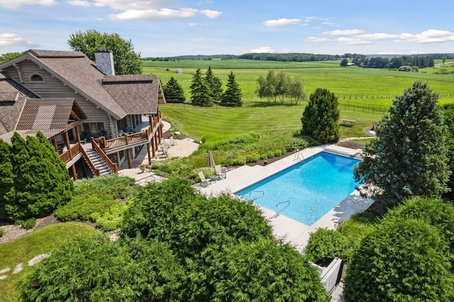 view of pool with a deck, a rural view, a patio area, and a lawn