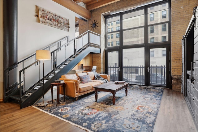 living room with brick wall, dark hardwood / wood-style floors, beam ceiling, and a towering ceiling