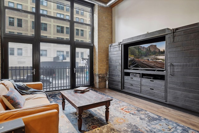 living room with light wood-type flooring, beamed ceiling, plenty of natural light, a towering ceiling, and a barn door