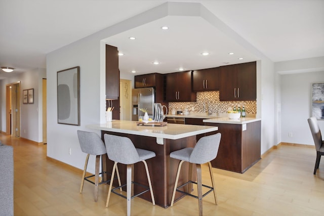 kitchen featuring a kitchen bar, light wood-type flooring, backsplash, kitchen peninsula, and stainless steel fridge