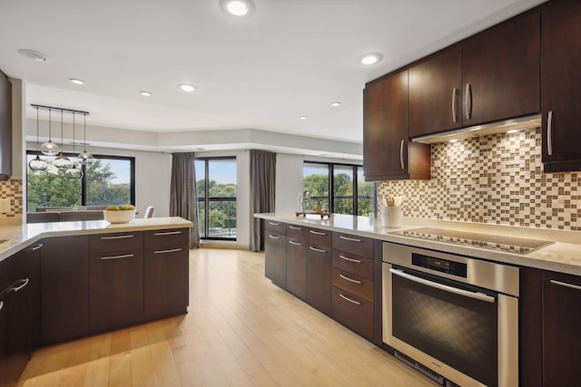 kitchen featuring tasteful backsplash, oven, light hardwood / wood-style floors, decorative light fixtures, and stovetop