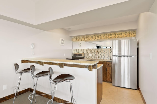 kitchen with light tile patterned flooring, a kitchen bar, backsplash, kitchen peninsula, and stainless steel appliances