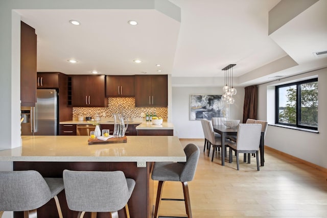 kitchen with light hardwood / wood-style flooring, kitchen peninsula, backsplash, a kitchen bar, and stainless steel refrigerator