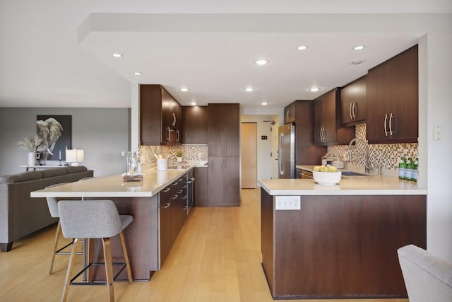 kitchen with a breakfast bar area, light hardwood / wood-style flooring, kitchen peninsula, stainless steel refrigerator, and tasteful backsplash