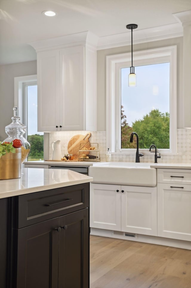 kitchen featuring decorative light fixtures, light hardwood / wood-style floors, tasteful backsplash, white cabinets, and crown molding