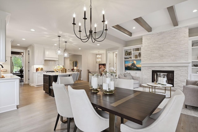 dining room with a chandelier, built in features, beam ceiling, a stone fireplace, and light wood-type flooring