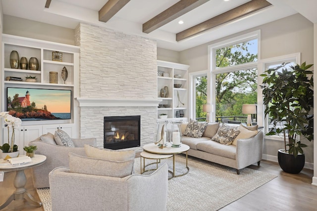 living room with beamed ceiling, a stone fireplace, and light wood-type flooring