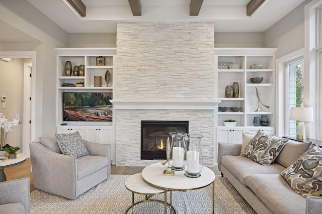 living room with beamed ceiling, built in features, a stone fireplace, and light hardwood / wood-style flooring