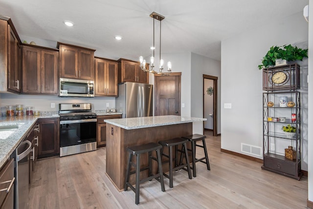 kitchen featuring light stone countertops, light hardwood / wood-style flooring, appliances with stainless steel finishes, and an inviting chandelier