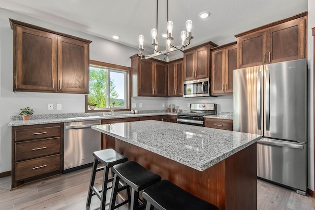 kitchen with light stone countertops, a chandelier, light hardwood / wood-style flooring, and stainless steel appliances