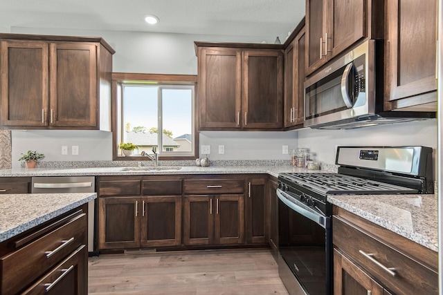 kitchen with sink, light stone counters, dark brown cabinets, appliances with stainless steel finishes, and light hardwood / wood-style floors