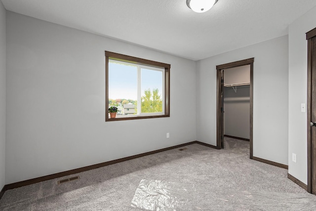 unfurnished bedroom featuring a spacious closet, light colored carpet, and a closet