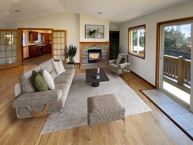 living room with french doors, light hardwood / wood-style flooring, vaulted ceiling, and a stone fireplace