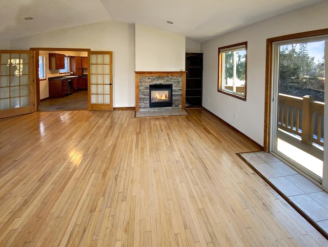 unfurnished living room with a fireplace, french doors, light hardwood / wood-style floors, and lofted ceiling