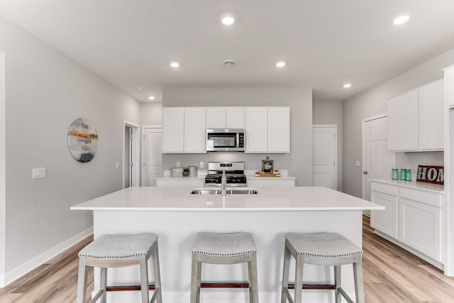 kitchen with an island with sink, a breakfast bar area, stainless steel appliances, light hardwood / wood-style floors, and white cabinetry