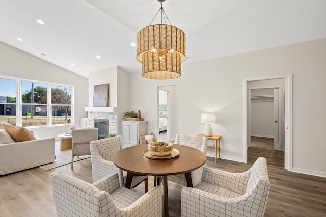 dining space featuring a stone fireplace, hardwood / wood-style flooring, and vaulted ceiling