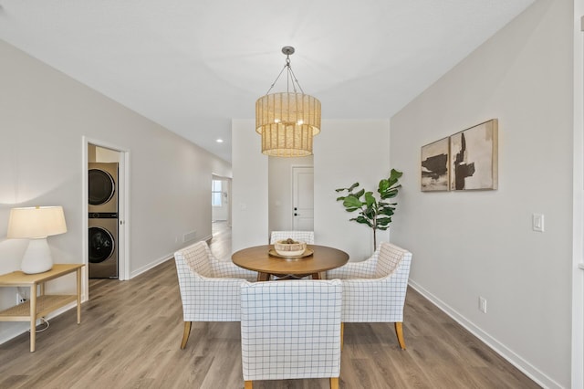 dining space featuring wood-type flooring, a chandelier, and stacked washing maching and dryer