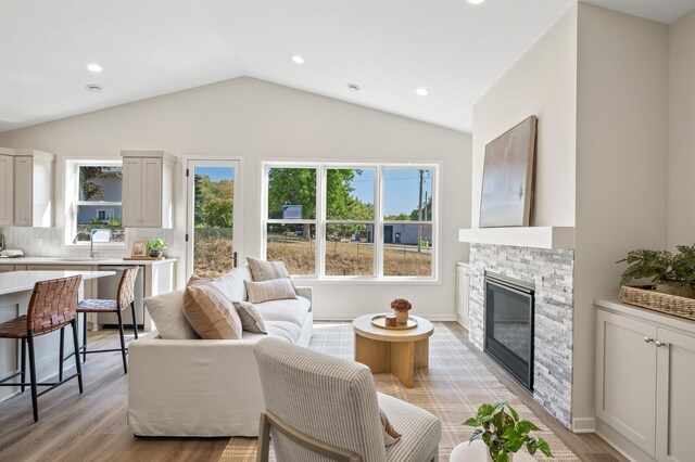 living room with sink, light hardwood / wood-style flooring, a fireplace, and vaulted ceiling