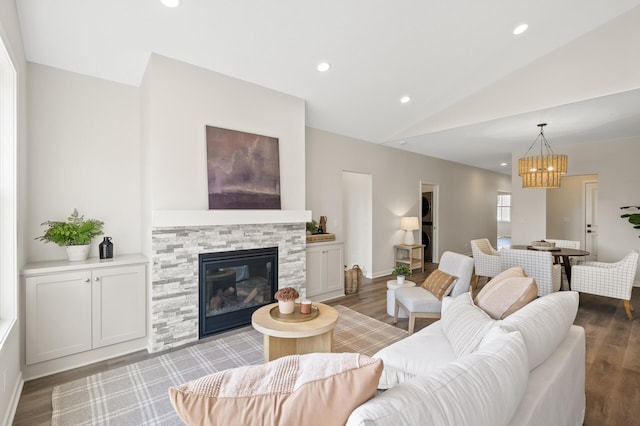 living room with an inviting chandelier, wood-type flooring, lofted ceiling, and a stone fireplace