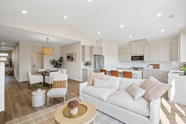 living room with light hardwood / wood-style flooring, vaulted ceiling, a chandelier, and sink