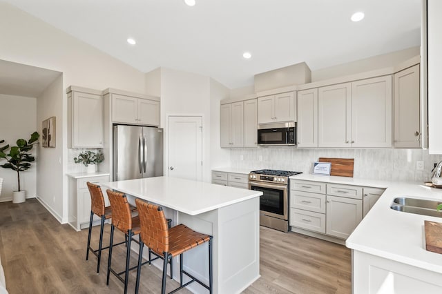 kitchen featuring a breakfast bar, stainless steel appliances, vaulted ceiling, and light hardwood / wood-style floors