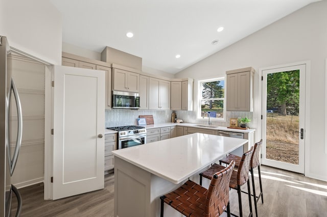 kitchen with light hardwood / wood-style floors, tasteful backsplash, vaulted ceiling, a kitchen island, and stainless steel appliances