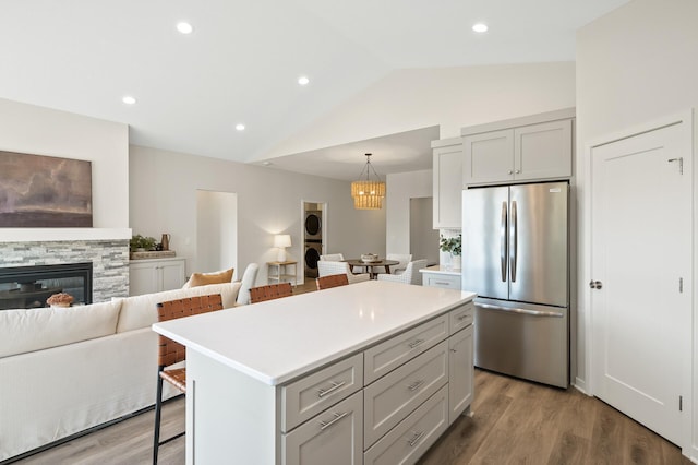 kitchen with stainless steel fridge, a breakfast bar, light wood-type flooring, lofted ceiling, and a center island