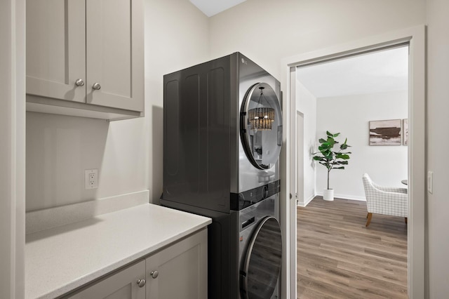 clothes washing area with cabinets, light hardwood / wood-style floors, and stacked washing maching and dryer