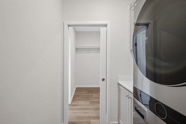 laundry room featuring light hardwood / wood-style flooring, cabinets, and stacked washing maching and dryer