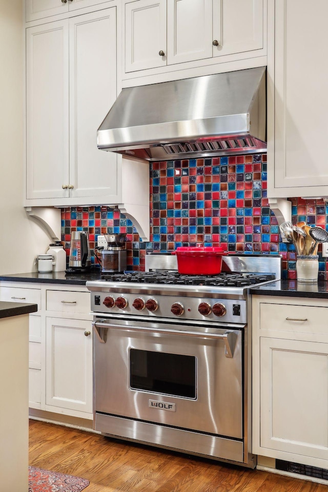 kitchen featuring tasteful backsplash, ventilation hood, luxury stove, light hardwood / wood-style flooring, and white cabinets