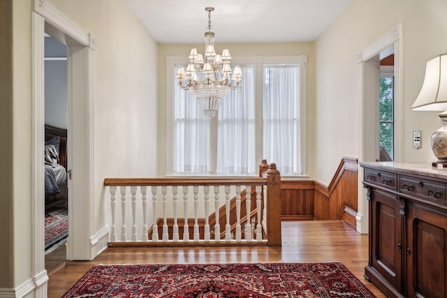 hall featuring light hardwood / wood-style floors, an inviting chandelier, and wood walls