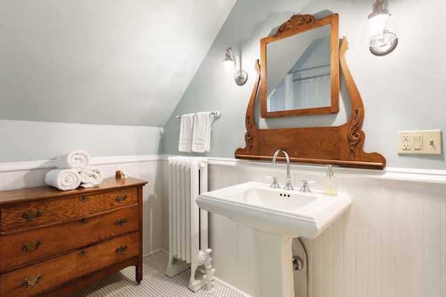 bathroom featuring vaulted ceiling, radiator, wood walls, and sink