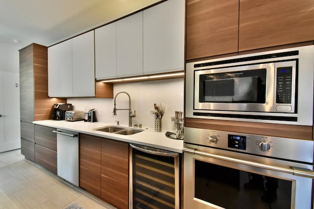 kitchen with appliances with stainless steel finishes, light tile floors, beverage cooler, sink, and white cabinetry