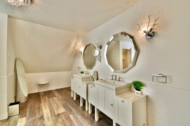 bathroom with a textured ceiling, wood-type flooring, dual vanity, and lofted ceiling