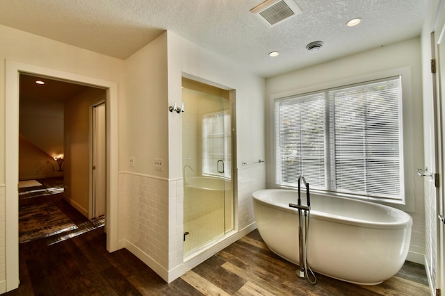 bathroom with a textured ceiling, plus walk in shower, and wood-type flooring