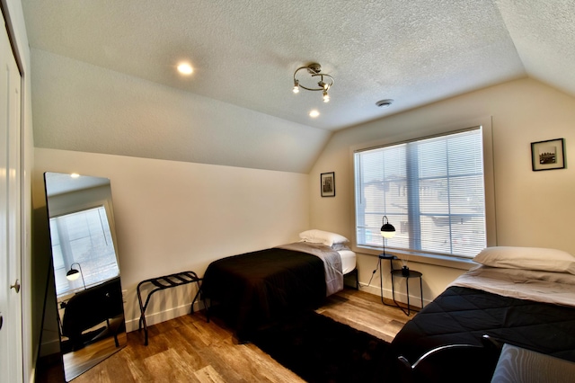 bedroom with lofted ceiling, light wood-type flooring, and a textured ceiling