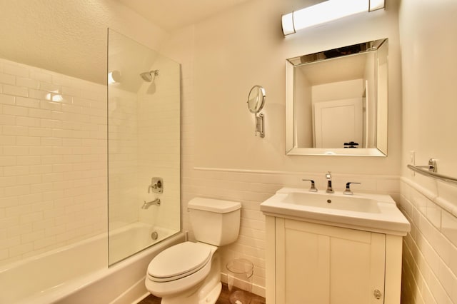 full bathroom with tile walls, tiled shower / bath combo, vanity, and toilet