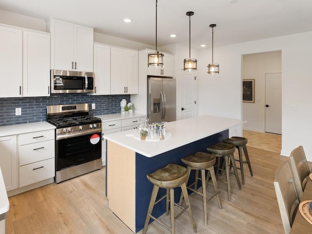 kitchen with a kitchen island, appliances with stainless steel finishes, a breakfast bar area, white cabinets, and light wood-type flooring