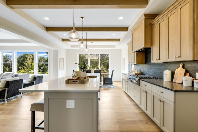 kitchen featuring backsplash, pendant lighting, stainless steel gas stovetop, light brown cabinetry, and a center island with sink