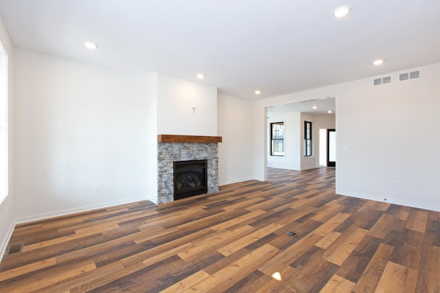 unfurnished living room featuring a stone fireplace and dark hardwood / wood-style floors