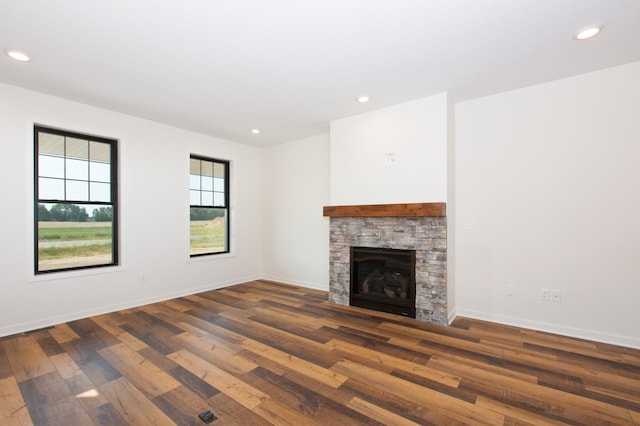 unfurnished living room with a stone fireplace and dark wood-type flooring