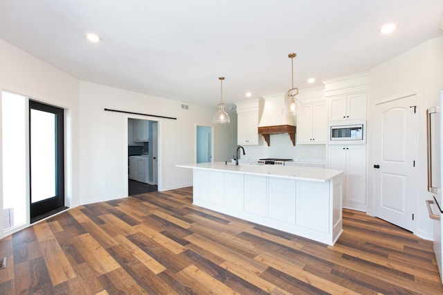 kitchen with dark hardwood / wood-style floors, stainless steel microwave, a center island with sink, premium range hood, and white cabinetry