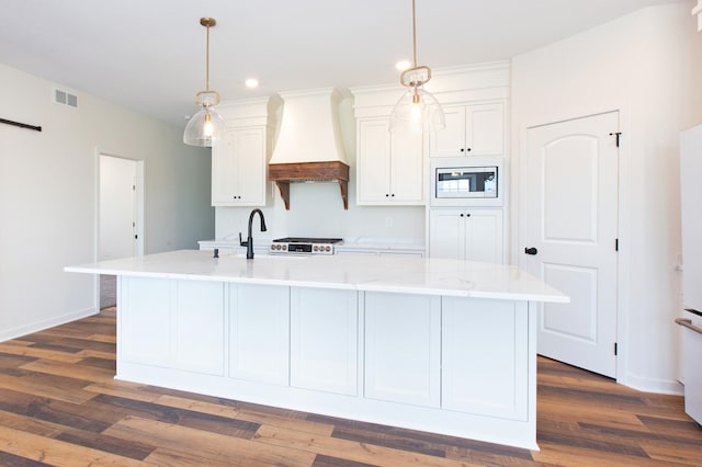 kitchen featuring a center island with sink, custom range hood, stainless steel microwave, and dark hardwood / wood-style floors