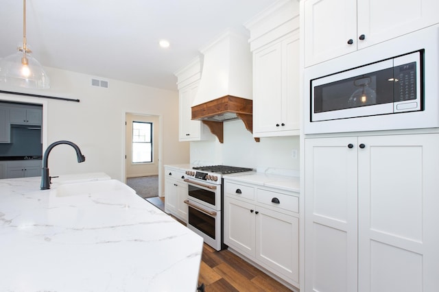 kitchen with stainless steel microwave, premium range hood, range with two ovens, and white cabinetry