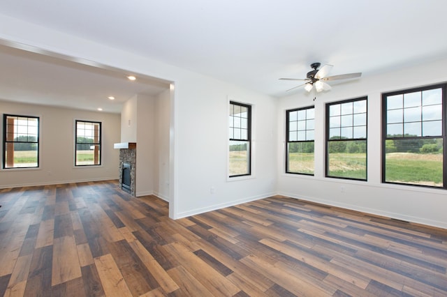 unfurnished room featuring dark hardwood / wood-style flooring, ceiling fan, and a stone fireplace