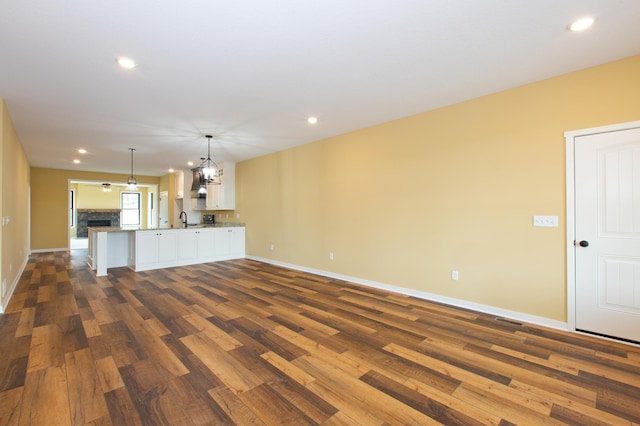 unfurnished living room with a chandelier, dark wood-type flooring, and sink